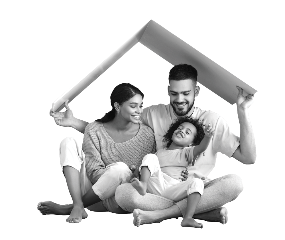 A couple sits closely on the ground as the man holds a piece of cardboard bent in the shape of a roof over their heads with their young child sitting in his lap.