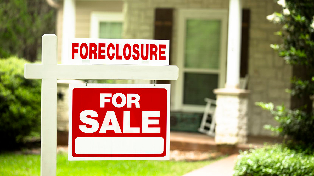 A foreclosure sign placed in the front lawn of a home in the background.
